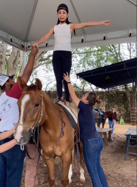Mulher em cima do cavalo com ajuda de profissionais